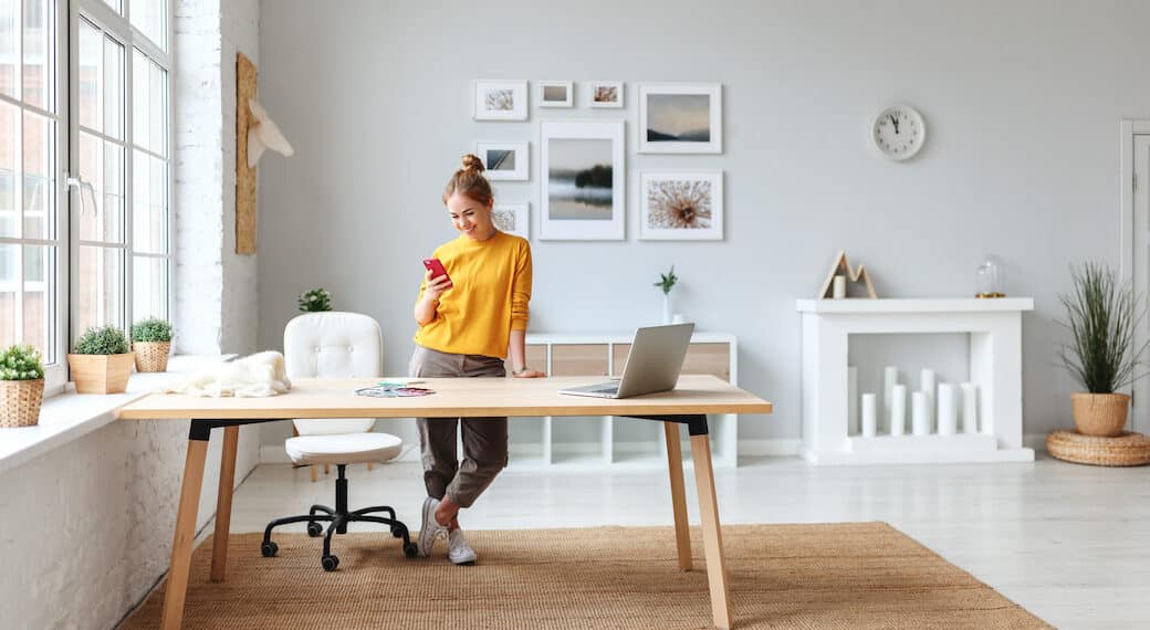creative young woman designer in a yellow sweater in the workplace at home in the interior of an apartment with large windows