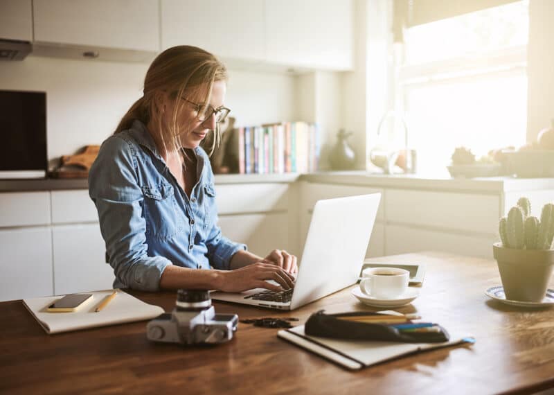 Female photographer sitting in her kitchen working on a laptop