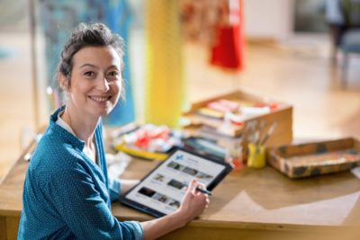 Smiling White woman working on iPad and sitting at desk in painting studio