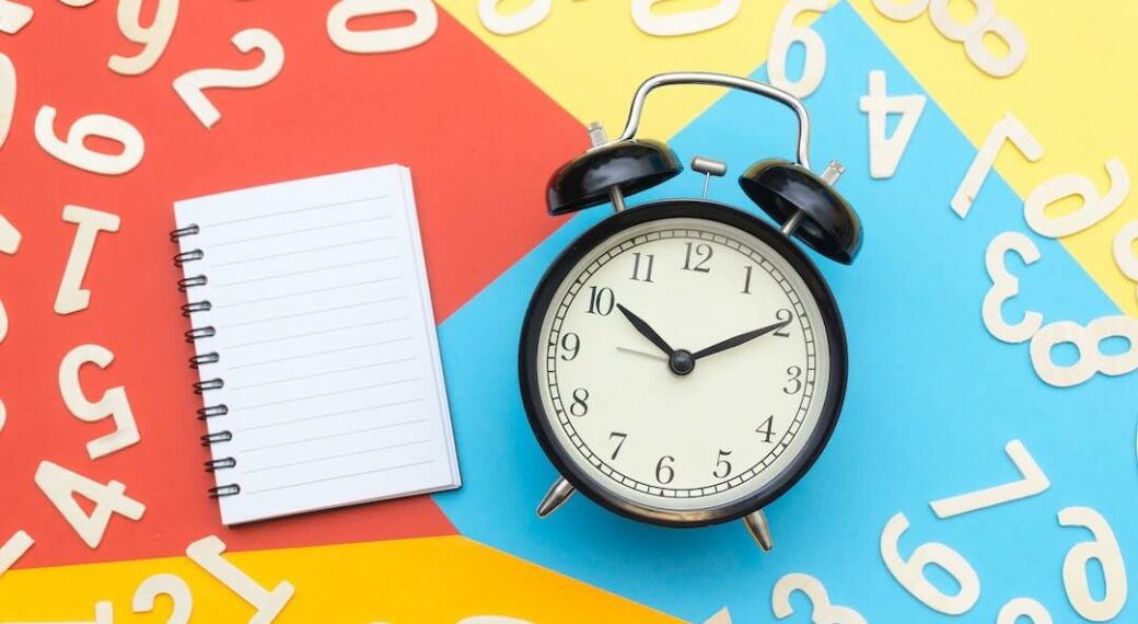 Old fashioned black clock and notebook on brightly colored background with white numbers