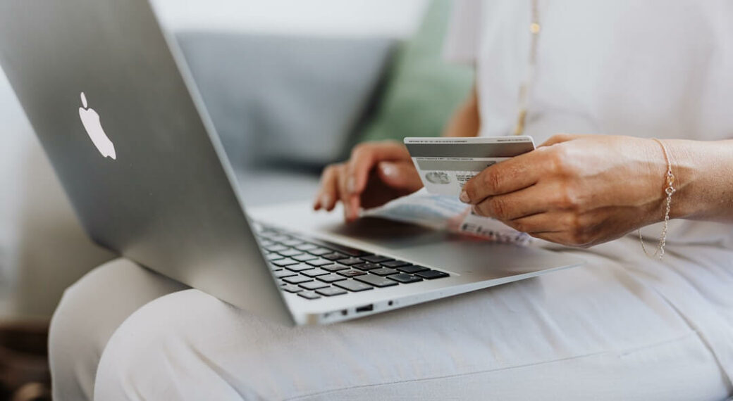Woman wearing all white sitting with a laptop on her lap holding a credit card