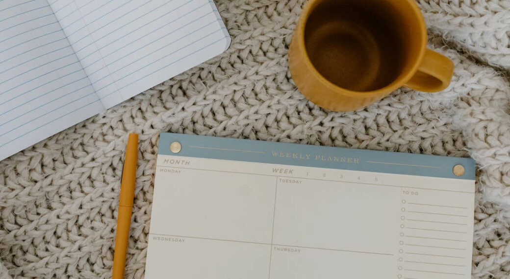 Mug, to-do list, and notebook on a white woven blanket.