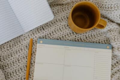 Mug, to-do list, and notebook on a white woven blanket.